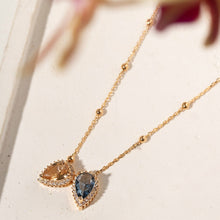 Cargar imagen en el visor de la galería, El collar con escapulario en forma de lágrima combina el azul intenso del cristal London Blue con el sofisticado brillo del cristal de citrino en una composición elegante y moderna. Con 70 cm de largo, baño de oro de 18 quilates e incrustaciones de circonita cúbica blanca, la pieza crea un aspecto ligero y refinado. El contraste de colores hace que el escapulario sea llamativo, luminoso y lleno de personalidad.
